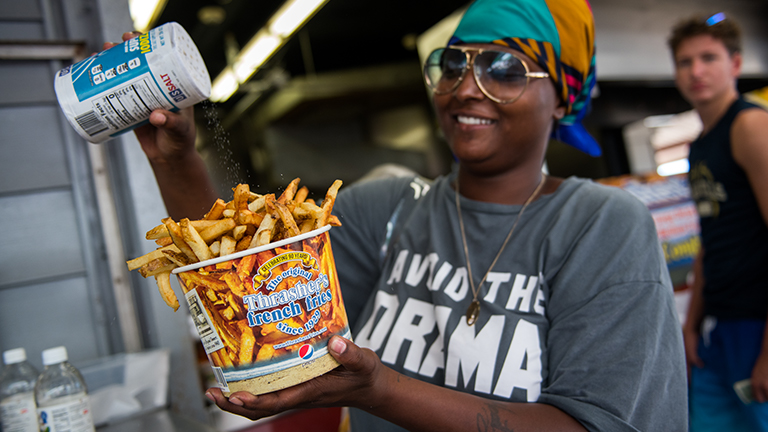 Young lady adding salt to her bucket of delicious Thrasher Fries on the Ocean City Boardwalk