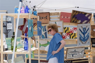 A woman looks at artwork in an outdoor booth. Photo
