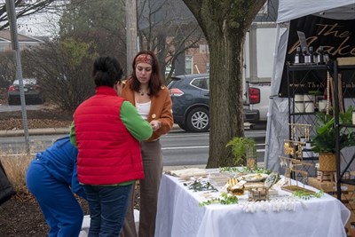 A woman talks with another woman about jewelry for sale at an outdoor booth. Photo
