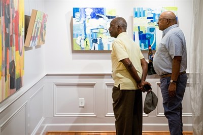 Photo of two men in Mansion gallery, gazing at artwork on wall. Photo