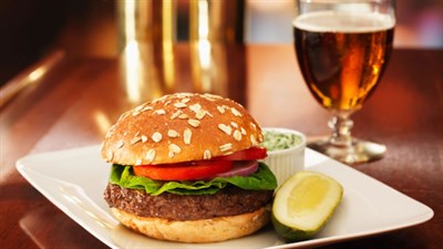A tasty burger with tomato, lettuce and onion joined with a pickle, cole slaw and a cold beer. Photo