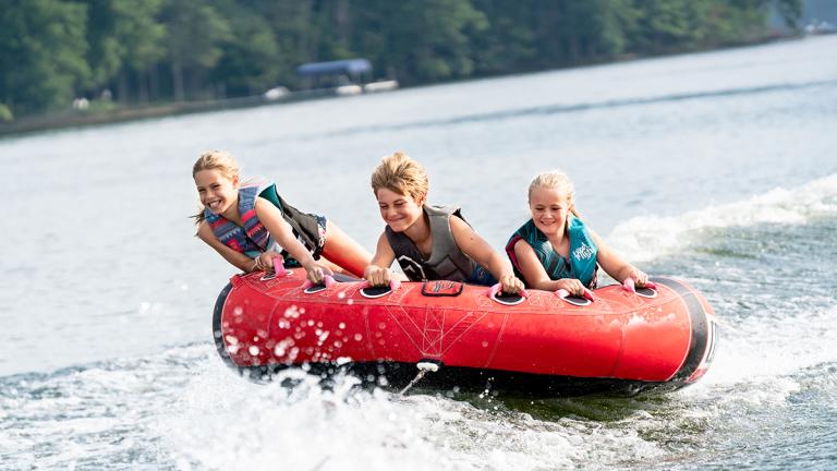 Three children being pulled around on a red water tube.