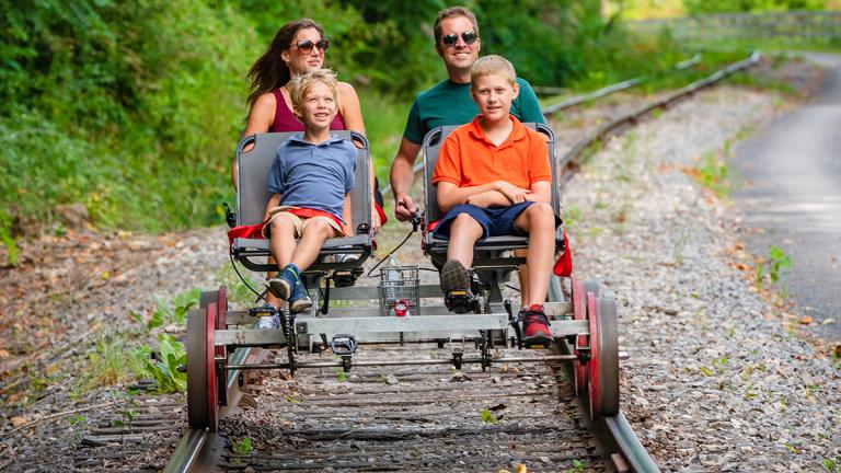 A family of four traveling down a railroad track on a pedal cart