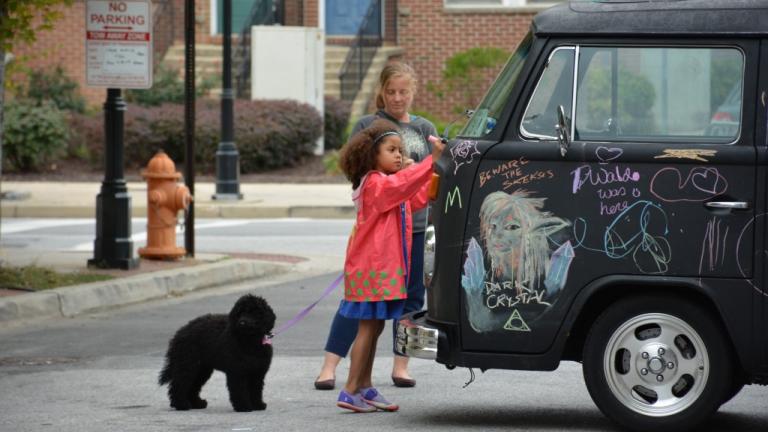 Young girls drawing on a car with a puppy at Madonnari arts festival