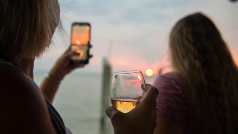 Woman Takes Photo of Sunset While Drinking Wine
