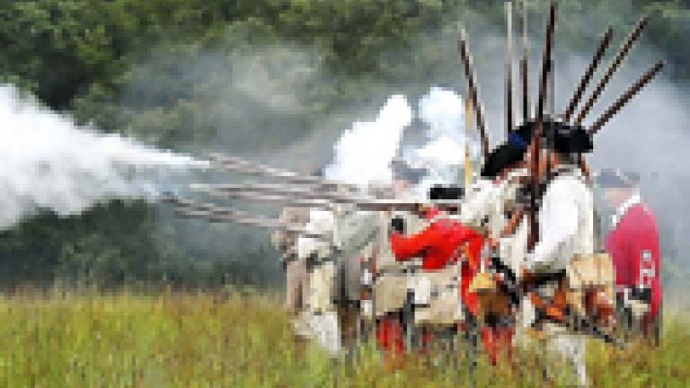 18th Century French, Indian and British reenactors lined up firing their rifles