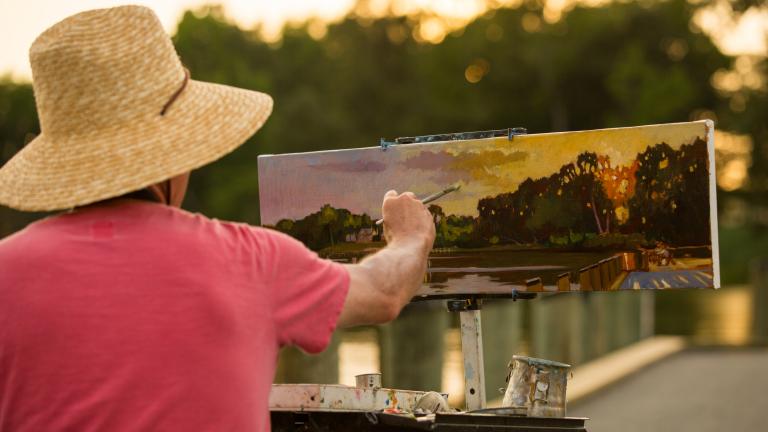 Photo looking over the shoulder of an Artist painting a landscape