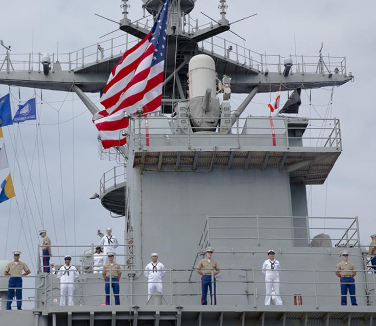 Naval Ship USS Oak Hill with Navy and Marine crew members at Parade Rest on deck.