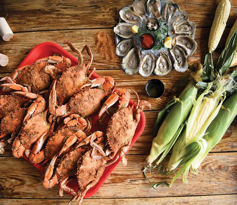 A tray of steamed crabs with a platter of steamed oysters on the half-shell and a few ears of corn.