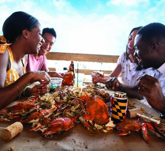 Four people smiling and enjoying their hot steamed Maryland crabs