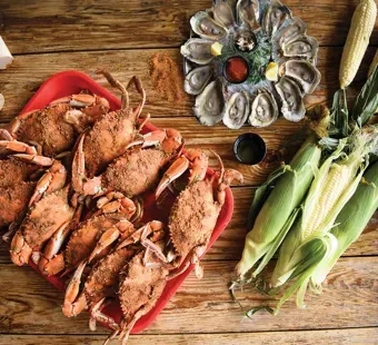 A tray of steamed crabs with a platter of steamed oysters on the half-shell and a few ears of corn.