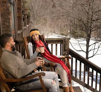 Couple sitting on a porch enjoying the snow and a cup of hot chocolate.