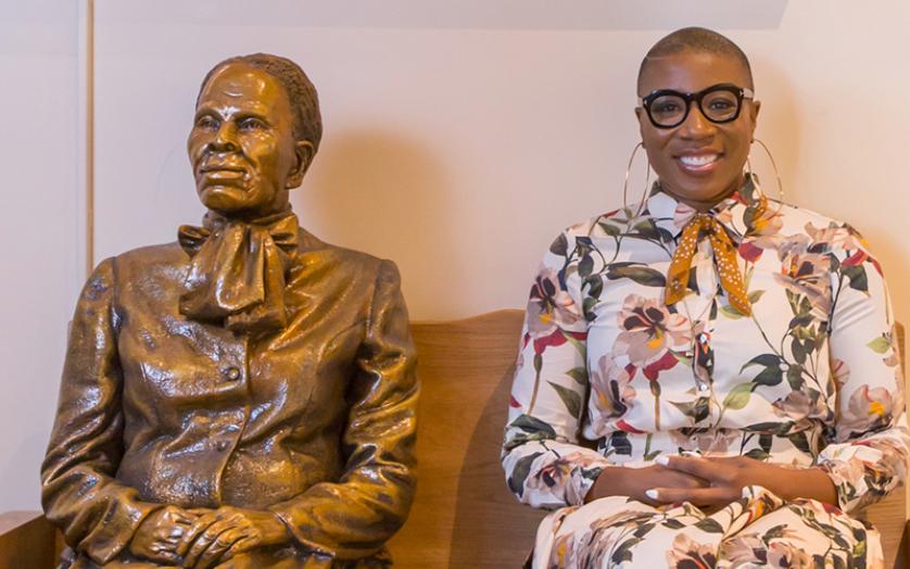 Actress Aisha Hinds sitting next to statue of Harriet Tubman