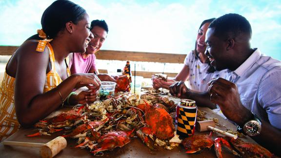 Four people smiling and enjoying their hot steamed Maryland crabs
