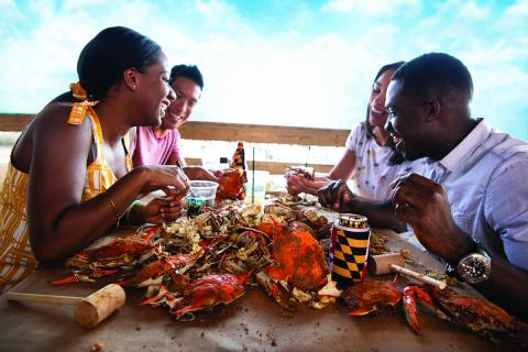 Four people smiling and enjoying their hot steamed Maryland crabs