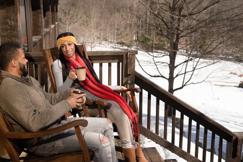 A Couple Enoying the Winter Snow, and A Cup of Hot Chocolate While Sitting on a Porch.