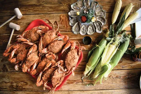 A tray of steamed crabs with a platter of steamed oysters on the half-shell and a few ears of corn.