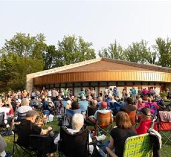 People sit on a lawn outdoors listening to am musical performance Photo