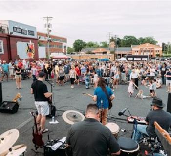 A band plays to a crowd of onlookers in a parking lot. Photo