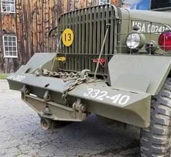 The grill of a 1940s jeep beside a historic wooden structure. Photo