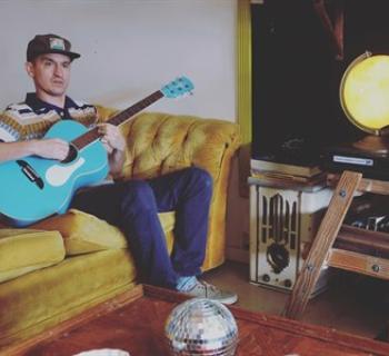 Wax sitting on a couch playing a guitar Photo