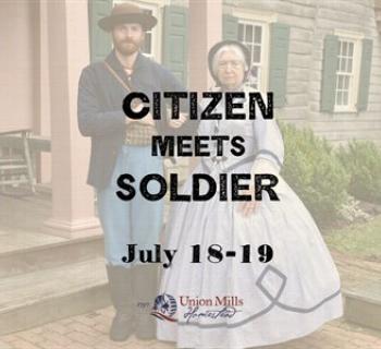 A Civil War soldier stands arm in arm with a woman in period dress in front of a historic house. Photo