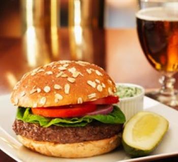 A tasty burger with tomato, lettuce and onion joined with a pickle, cole slaw and a cold beer. Photo