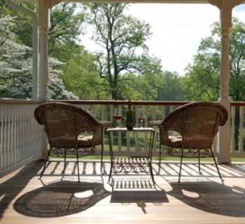 Two chairs and a table with a bottle of wine and two glasses on a porch at the Thanksgiving Farm. Photo