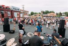 A band plays to a crowd of onlookers in a parking lot. Photo