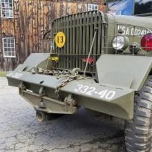 The grill of a 1940s jeep beside a historic wooden structure. Photo