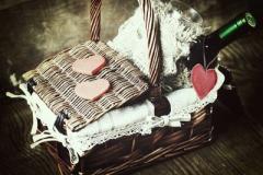 Picture os a basket with a bottle of wine and some pink heart shaped chocolates on top