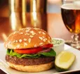A tasty burger with tomato, lettuce and onion joined with a pickle, cole slaw and a cold beer. Photo