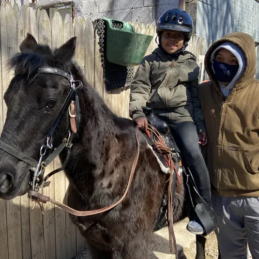A man stands next to his son on a horse at the Carlton Street Stables