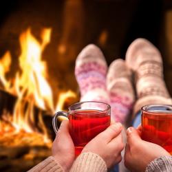 Couple holding glasses of mulled wine in front of fireplace Photo